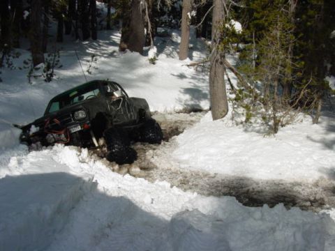 1986 Ford Bronco - Off-road pickup truck with large tires stuck in a snowy ditch during winter.
