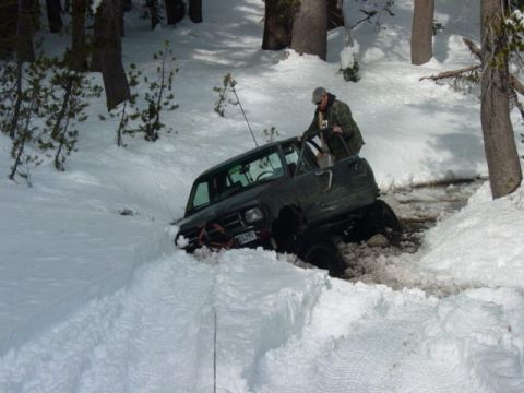 1986 Ford Bronco - A person is getting out of an off-road vehicle that is stuck in a snowy ditch.