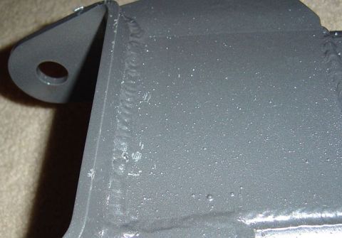 1986 Ford Bronco - Close-up of a freshly gray-painted fabricated steel bracket showing stacked weld beads along its seams and a rounded tab with a bolt hole,…
