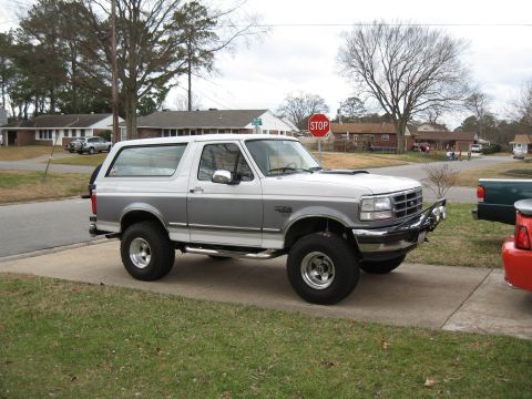 1994 Ford Bronco - A two-tone white and gray Ford Bronco is parked on a concrete driveway in a suburban neighborhood.