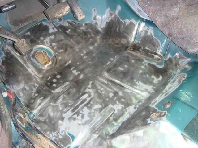 Vehicle interior floor undergoing rust repair, showing pedals and brake release lever