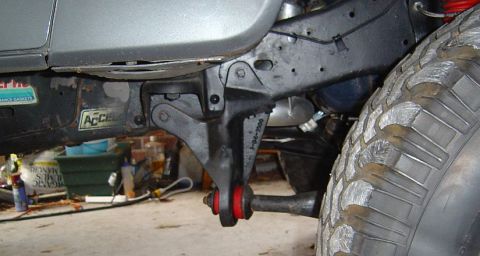 1986 Ford Bronco - Close-up underside view of a vehicle's front frame area showing a black-painted bracket or mount with a red-and-black polyurethane bushing…