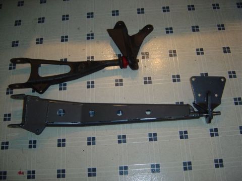 1986 Ford Bronco - Two automotive suspension/frame brackets shown for comparison on a tiled floor: an older worn dark bracket with a red-tipped bushing at top…