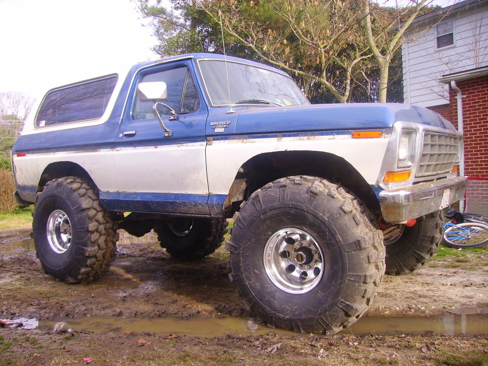 Blue and white 1978 Ford Bronco with large off-road tires, 3/4 front view