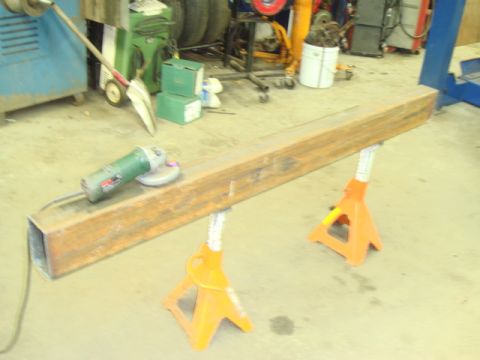 1996 Ford Bronco - Metal beam on jack stands with an angle grinder, workshop background.