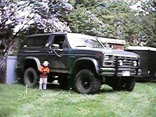 1986 Ford Bronco - This Ford Bronco is parked outdoors on a grassy area, with trees and structures in the background.