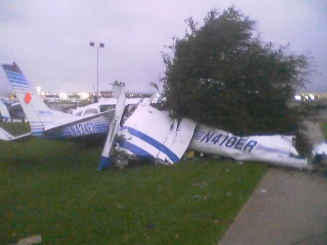 Damaged small aircraft including one marked N410ER lying on grass beside a walkway