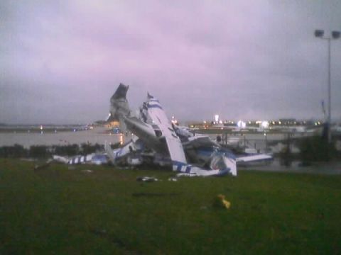 1989 Ford Bronco - Damaged airplane wreckage on a field near an airport runway.