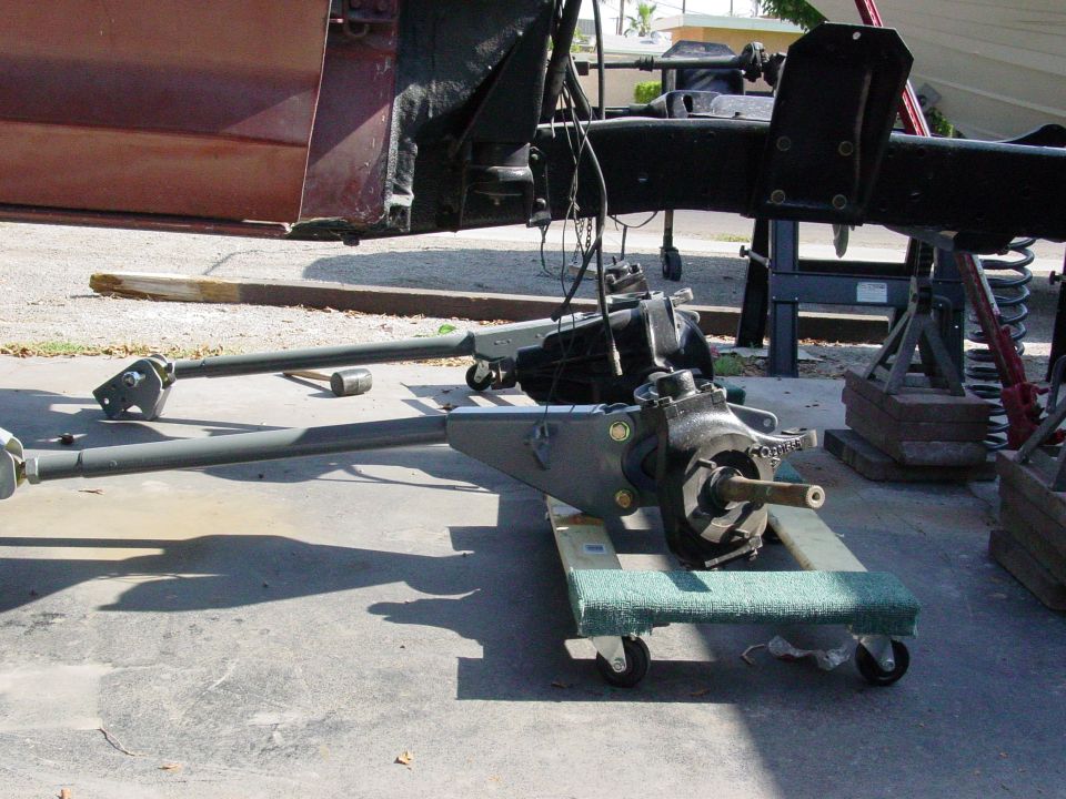 Vehicle chassis and suspension parts on dollies, with a maroon door in the background