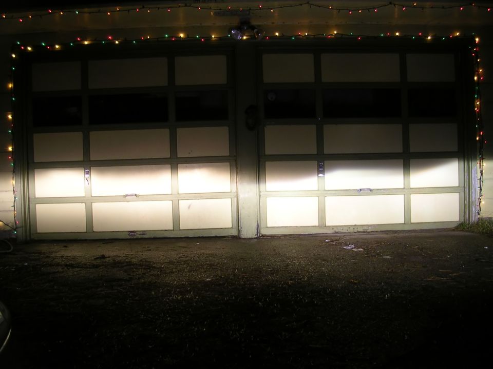 Two garage doors illuminated by headlights, with colorful string lights overhead