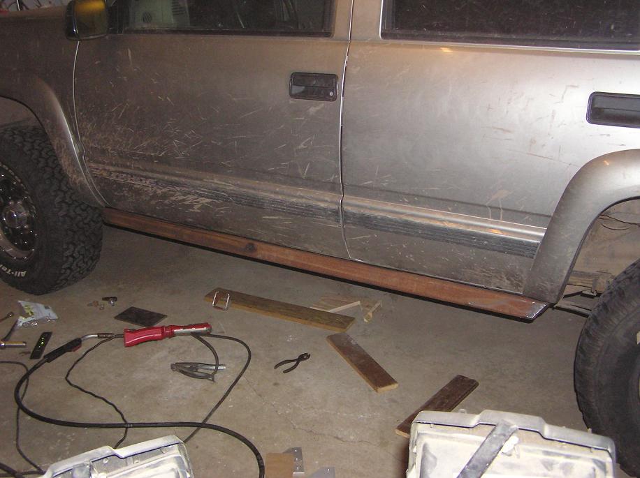 Tan Chevy SUV in garage with bare steel rock slider tacked to rocker, welder on the floor