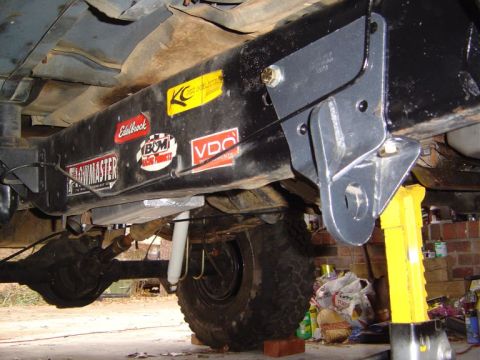 1986 Ford Bronco - Underside view of a black-framed vehicle chassis, showing suspension components, a differential, an off-road tire, and various decal sticke…
