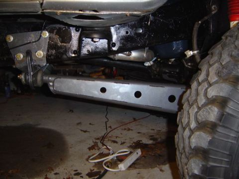 1986 Ford Bronco - Underside view of a truck/SUV frame showing a freshly installed bare-metal steel skid plate or crossmember with three drilled holes, mounte…