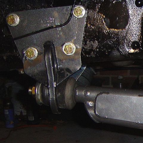 1986 Ford Bronco - Close-up underside view of a steel bracket or mount plate secured with several gold zinc-plated hex bolts, connecting to a driveshaft or st…