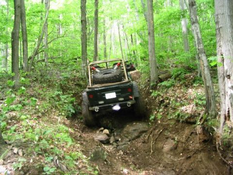 1986 Ford Bronco - An off-road vehicle navigates a challenging dirt path through a dense forest.