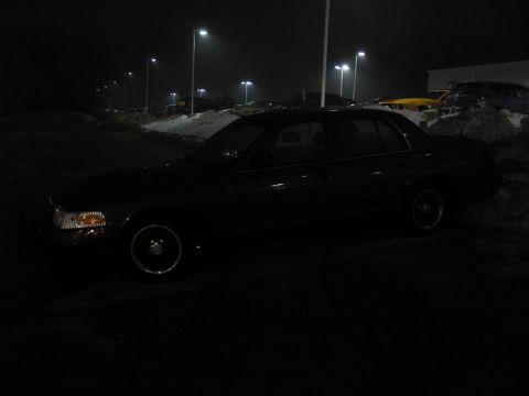 2001 Ford Crown Victoria - A dark sedan sits parked in a lot under streetlights at night.