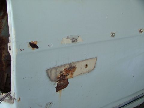 1969 Ford Ranchero - Detail of a heavily rusted tailgate latch mechanism on a light blue vehicle, showing signs of wear and tear.