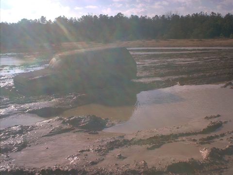 1978 Ford Bronco - A dark-colored SUV is buried up to its windows in a large mud pit, viewed from the front-left as it churns through deep muddy water. Heavy…
