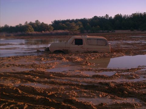 1978 Ford Bronco - A tan 1978 Ford Bronco is deeply stuck in a muddy, watery landscape under a pale sky.