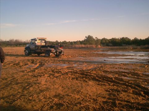1978 Ford Bronco - Tow truck is stuck in a muddy field with water and trees visible in the distance.