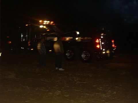 1978 Ford Bronco - A large truck is parked at night, illuminated by its own lights and two people stand beside it.