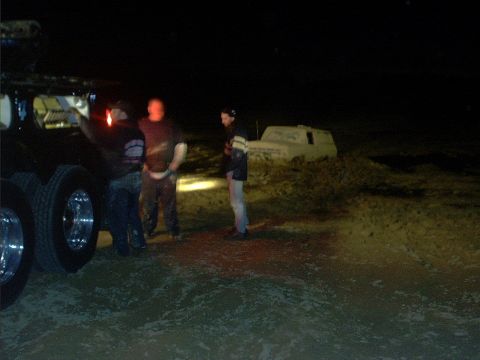 1978 Ford Bronco - Nighttime scene showing three people standing near a dark 4x4 with a front-mounted winch and chrome wheels on the left, while a light-color…