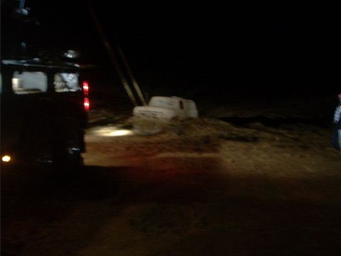 1978 Ford Bronco - Blurry night shot of a white full-size SUV buried to its rocker panels in a mud pit, lit by the marker lights and work lamps of a dark truc…