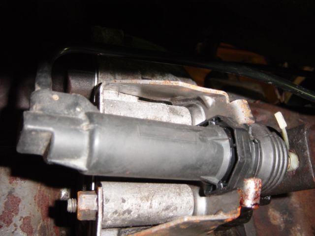 Close-up of an automotive part, possibly a clutch actuator or similar mechanism, with metal brackets and wiring
