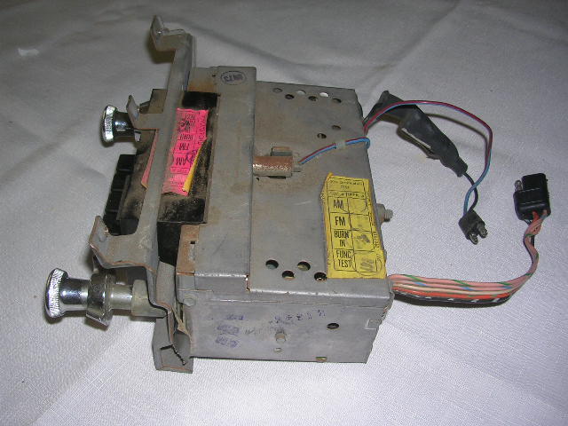 Car radio with two knobs, wiring harness, and fuse. Yellow sticker has AM/FM labels