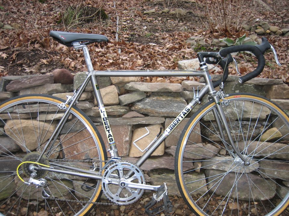 Silver 'LIBERTAS' road bike with gum-wall tires leaning on a stone wall