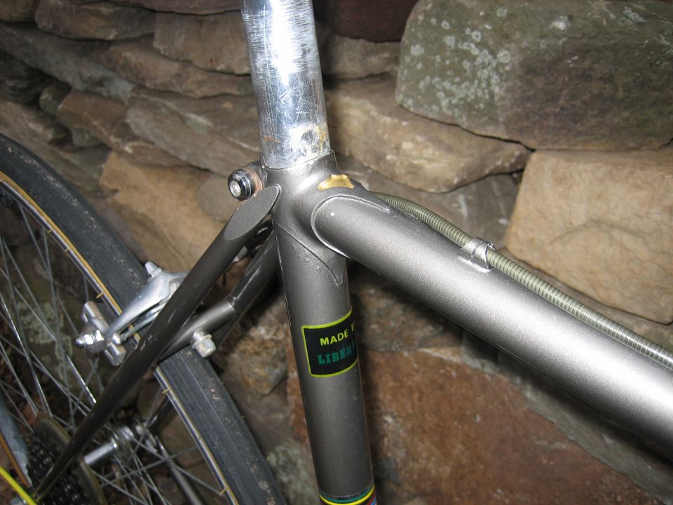 Close-up of gray bicycle frame lug and head tube against a stone wall