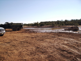 1978 Ford Bronco - Two trucks are stuck in a muddy field with trees in the background.