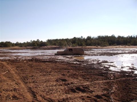 1978 Ford Bronco - A vehicle is submerged in mud, with tire tracks visible in the foreground.