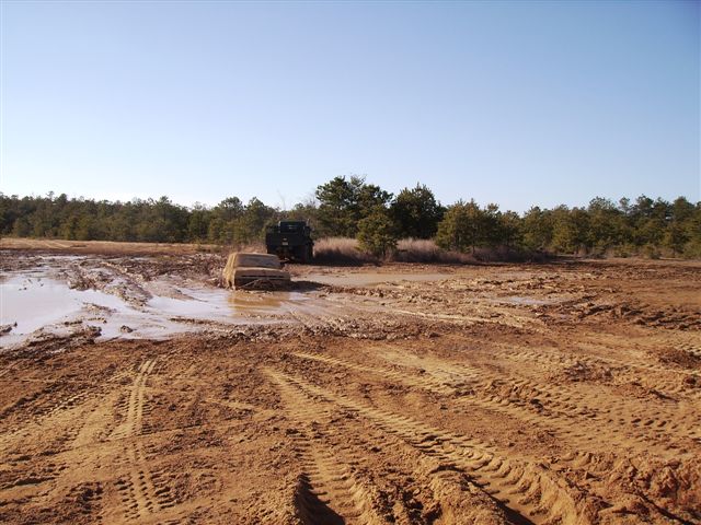 Tan SUV stuck in mud, with a dark vehicle behind it
