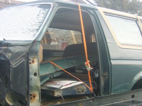1990 Ford Bronco - This green Ford Bronco, likely from the late 1980s, is being transported on a trailer with its door ajar and secured by straps.