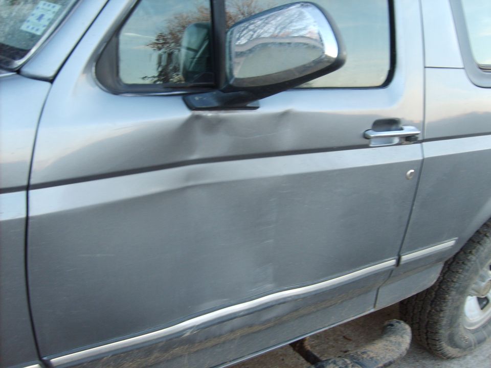 Silver SUV door with significant denting near the handle and along the body line