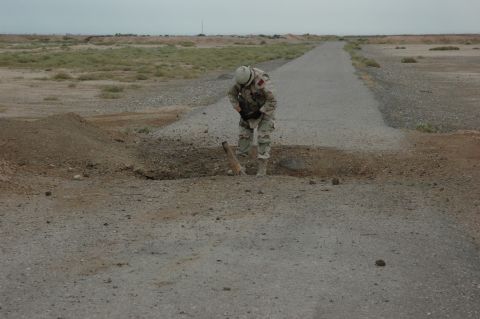 1996 Ford Probe - A soldier inspects a piece of unexploded ordnance on a desolate road in a barren landscape.