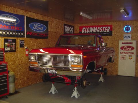 1978 Ford Bronco - A red 1978 Ford Bronco is elevated on jack stands in a garage, displaying its front grille and suspension.