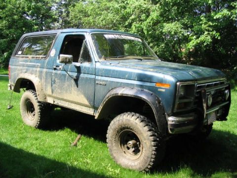 1986 Ford Bronco - This is a blue Ford Bronco with off-road tires, parked on grass and covered in dirt.
