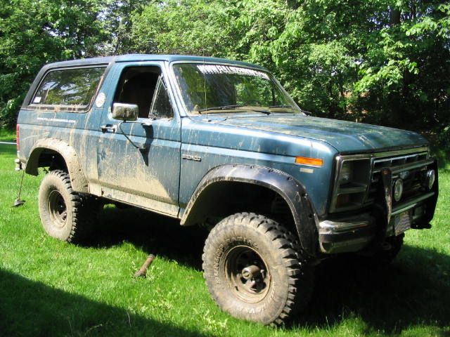 Muddy blue Ford Bronco with fender flares and grille guard on grass