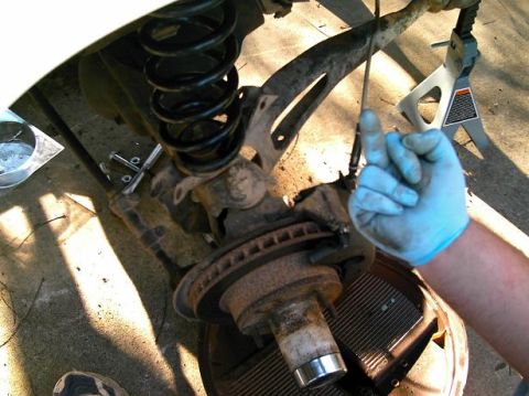 1986 Ford Bronco - A mechanic's gloved hand points to a vehicle's suspension and brake system during a repair.