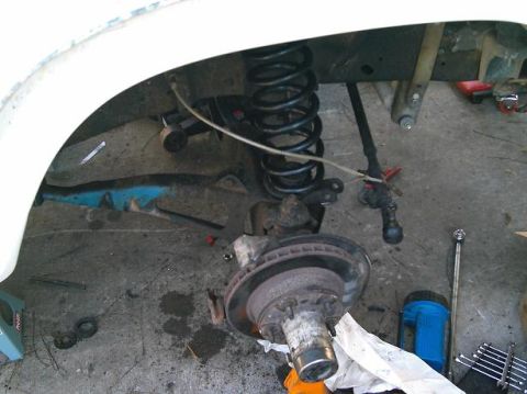 1986 Ford Bronco - Close-up view of a vehicle's suspension system, including a coil spring and brake assembly, with tools scattered around.