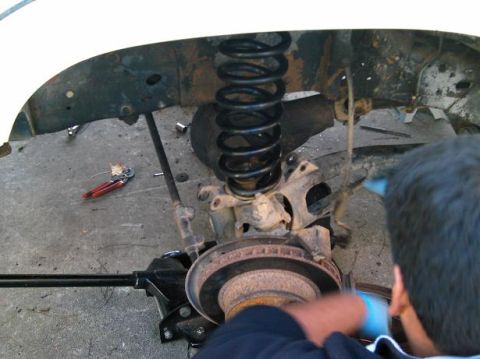 1986 Ford Bronco - Mechanic working on vehicle suspension components, showing a coil spring and brake assembly.