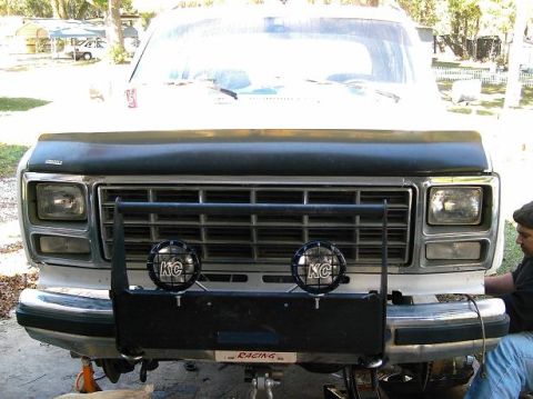 1986 Ford Bronco - This truck features a prominent grille and auxiliary lights, with a person working on the front end.