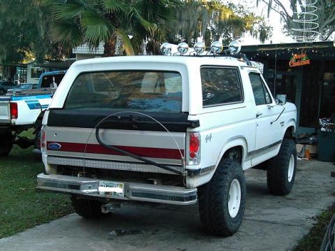 1986 Ford Bronco - White Ford Bronco with lifted suspension and off-road tires, parked next to a blue and white pickup truck.