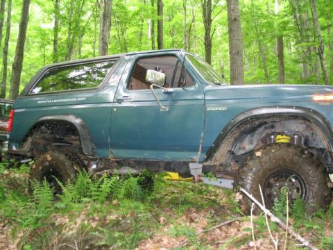 1986 Ford Bronco - This 1986 Ford Bronco is shown off-road in a forest with mud on its tires and body.