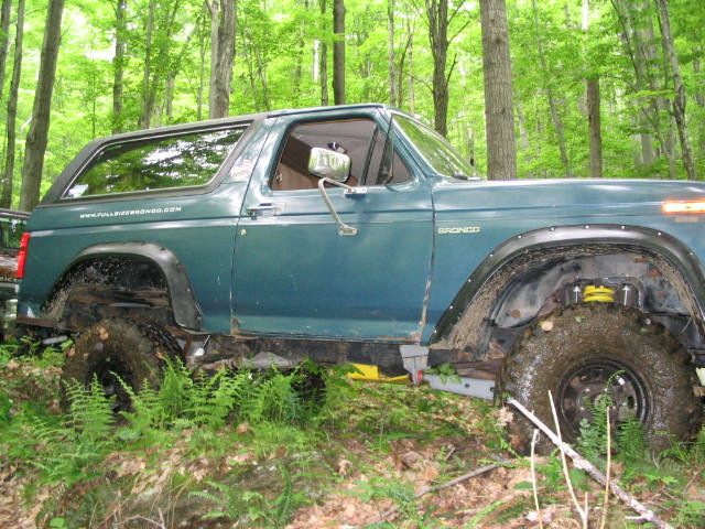Green Ford Bronco with lifted suspension and large tires driving through a wooded area