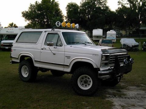 1986 Ford Bronco - A white Ford Bronco with a lifted suspension and off-road tires sits on a grassy field.