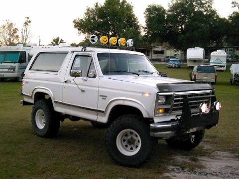1986 Ford Bronco - White Ford Bronco with lifted suspension and off-road tires parked outdoors with other vehicles and RVs.