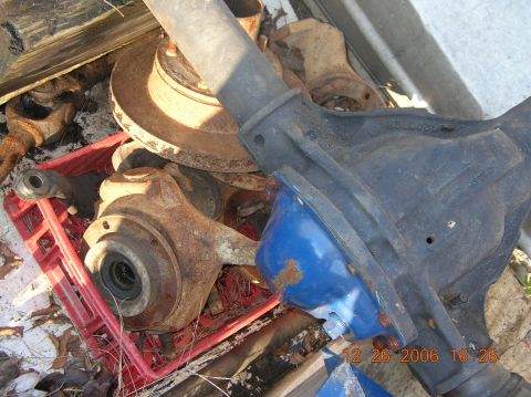1991 Ford F-150 - Various rusty vehicle axle components are piled together, some in a red crate.